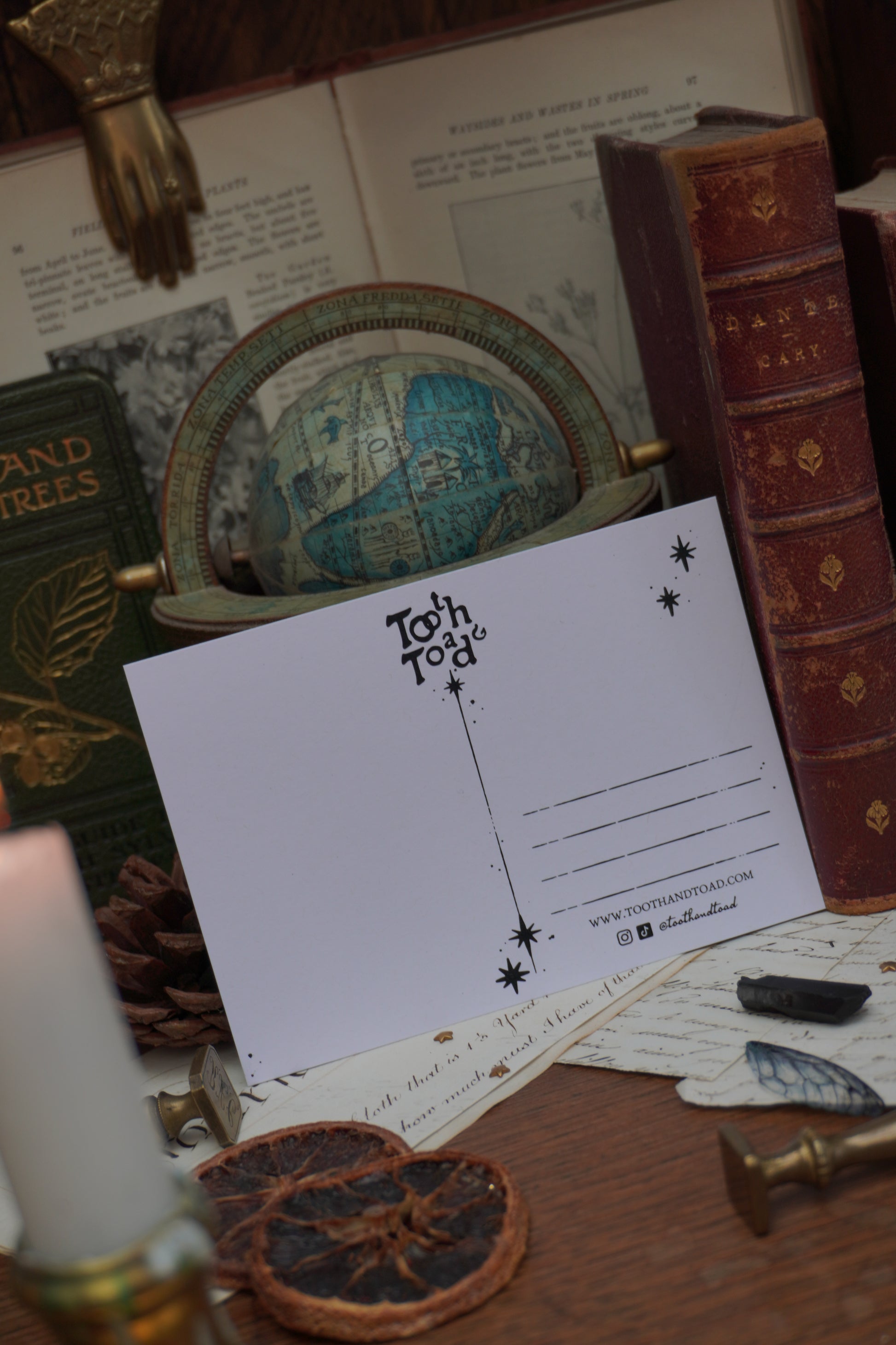 A white postcard with black text, Tooth and Toad logo and stars against a background of vintage decorative elements, old books and a globe